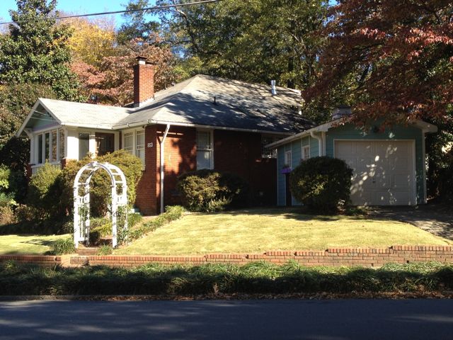 The front of 853 Euclid Ave in autumn: a 1930 brick bungalow set back from the street, a white wooden rose arbor at the front walk, a green-trimmed garage on the right, and copper-yellow leaves overhead.